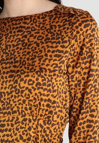 Leopardskinnetop i orange och mörkbrunt, tillverkat av mjukt tyg. Har en rund halsringning och diskret samling vid midjan.