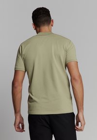 Groene polo-shirt met korte mouwen, van een lichte tint en zachte textuur, met een geribde kraag en slim fit, gezien van de achterkant tegen een vlakke achtergrond.