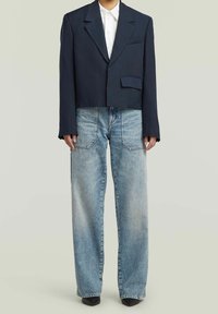 Blazer de marinero recortado con solapas en pico sobre una camisa blanca de botones, combinado con jeans de pierna ancha en azul claro y zapatos de tacón negros.