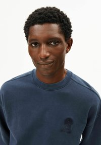 Marineblauwe sweatshirt met een ronde hals, gestructureerde stof en een opvallend geborduurd keyhole-ontwerp op de linkerbovenzijde van de borst.