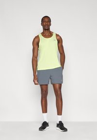 Αθλητική φανέλα ανοιχτού πράσινου χρώματος με στρογγυλή λαιμόκοψη, συνδυασμένη με γκρι σορτς. Σύντομο σχέδιο, κατασκευασμένο από αεριζόμενο ύφασμα. Μαύρα αθλητικά παπούτσια με λευκές λεπτομέρειες.