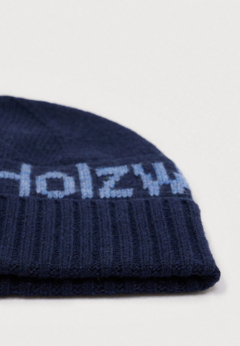 Berretto a maglia blu navy con texture a coste, caratterizzato da lettere del logo azzurro intorno al bordo. La parte superiore è leggermente arrotondata.