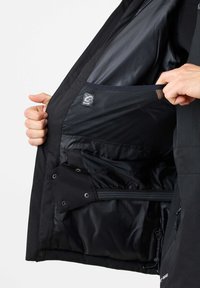 Schwarzes Jackeninnere mit einem glatten, glänzenden Futter. Verfügt über eine Netzinnentasche und ein Reißverschlussfach. Strukturierter Stoff mit Druckknopfverschlüssen.
