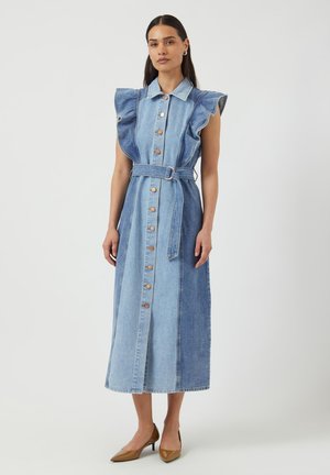 Sukienka dżinsowa z krótkimi falbanianymi rękawami, zapinana na guziki z przodu, z paskiem do wiązania. Charakteryzuje się blokami kolorów w jasnym i ciemnym odcieniu niebieskiego oraz długością midi.