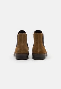Hnědé semišové kotníkové boty s elastickými bočními panely, hladkým tmavým vnitřním podšívkou a stohovaným podpatkem. Minimalistický a praktický design.