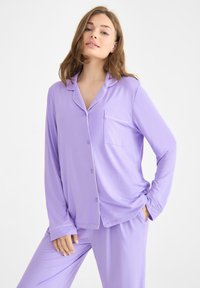 Ljuslila pyjamas set i mjukt tyg; har en knapplist skjorta med ficka och kontrasterande vit passpoal, i kombination med matchande byxor.
