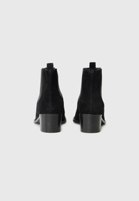Black suede ankle boots with a low heel, viewed from the back, featuring a sleek design and side elastic panels.