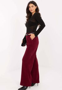 Czarny body z długim rękawem w połączeniu z bordowymi, szerokimi spodniami z wysokim stanem, wykonanymi z gładkiego materiału i wyposażonymi w pas w tym samym kolorze, noszony z czarnymi szpilkami.