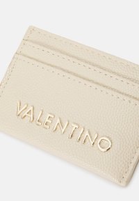 Beige textured leather cardholder with four slots, featuring embossed "VALENTINO" logo in gold metal, and neat stitching along the edges.