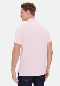 Polo de manga corta en rosa claro con cuello, fabricado en tela suave. Presenta una abertura lateral en el dobladillo y un detalle de costura minimalista.