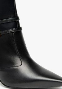 Stivale alla caviglia in pelle nera con punta affusolata, caratterizzato da un taglio verticale sottile, una cinturino avvolgente alla caviglia e una texture liscia e lucida.