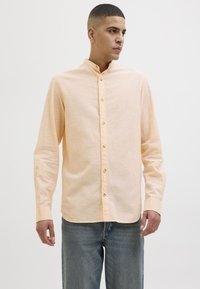 Lichtperzikkleurig shirt met lange mouwen, een mandarinokraag, knopen aan de voorkant en een zachte textuur, gecombineerd met blauwe denim jeans.