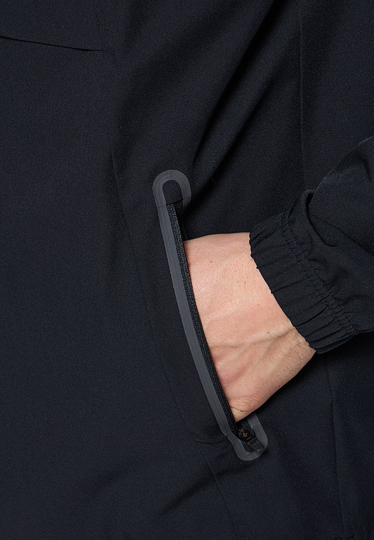 Veste noire avec une vue rapprochée d'une poche latérale. La poche zippée présente une fermeture éclair grise avec un tirette en matériau doux, mettant en valeur la texture et le design.