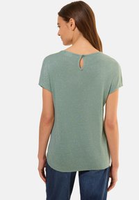 Haut vert à manches courtes avec une texture brillante. Il présente un détail au dos en forme de trou de serrure maintenu par un bouton. Coupe douce et décontractée.