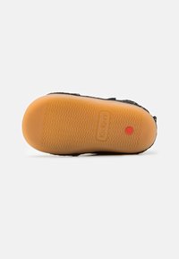 Semelle de chaussure en suède noir au design plat, avec un motif de grip en caoutchouc et un point rouge. La marque "Kickers" est embossée sur la semelle.