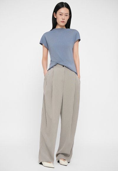 Jasnoniebieska koszulka z krótkim rękawem w połączeniu z szerokimi, szerokimi spodniami w paski w odcieniach beżu i szarości. Spodnie mają kieszenie z przodu i guzik. Białe spiczaste buty.