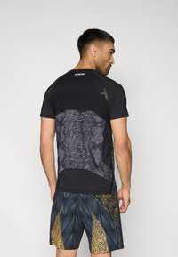 Μαύρο αθλητικό μπλουζάκι με υφή φιδιού στην πλάτη, συνδυασμένο με σορτς με μοτίβα σε σκούρες αποχρώσεις και χρυσές λεπτομέρειες.