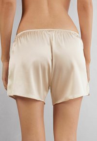 Seta-beiga satinsjorts med elastisk midjeband och lös passform, med en slät textur och något böjda nederkanter.