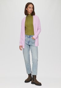 Lichtroze cardigan over een olijfgroen top, gecombineerd met lichtblauwe jeans en bruine enkellaarsjes, met een ontspannen pasvorm en geribbelde textuur.