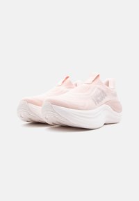 Αθλητικά παπούτσια σε ανοιχτό ροζ χρώμα με χοντρές λευκές σόλες, υφασμάτινα επάνω μέρη με υφή και λογότυπα στα πλάγια, παρουσιασμένα πάνω σε απλό φόντο.