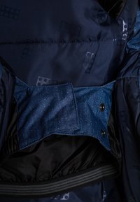 Interno di giacca blu scuro con fodera a motivo, vita elastica e cinturino in tessuto regolabile con bottone a pressione.