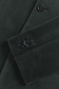 Tamsiai žalias švarkas iš minkštos, tekstūruotos medžiagos, su atplaiša apykakle ir keturiais juodais mygtukais rankovės gale su toniniu siuvinėjimo detalėmis.