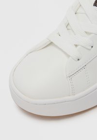 Bel bel usnjenih superg z zaobljenim sprednjim delom, ravnim podplatom in belimi vezalkami. Ima šive in teksturiran gumijast podplat.