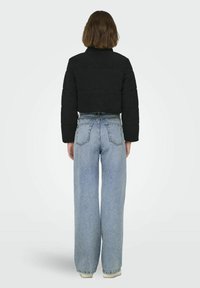 Zwarte cropped pufferjack met een gestructureerd, fleece-achtig materiaal. Gecombineerd met lichtblauwe high-waisted wijde spijkerbroeken.