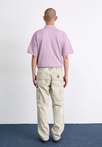 Hellblaues kurzärmliges Polohemd, kombiniert mit hellbeigen Cargo-Hosen, die mehrere Taschen und ein Logopatch auf der Rückseite haben.