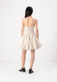 Robe sans manches de couleur beige clair avec un corsage ajusté, texture smockée et une jupe évasée. Elle dispose d'une fermeture éclair au dos et de bretelles fines.