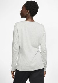 T-shirt a maniche lunghe grigio chiaro realizzato in tessuto morbido, con colletto rotondo e vestibilità rilassata, caratterizzato da una texture sottile. Pantaloni sportivi neri visibili sotto.