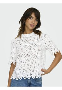 Weißes Baumwolloberteil mit ausgeschnittenem Blumenmuster, gewellten Kanten und kurzen Ärmeln. Texturiertes Design fügt Tiefe und visuelles Interesse hinzu.