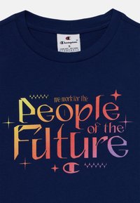 T-shirt de algodão azul-marinho com gráfico de texto colorido e estrelas, com a inscrição "trabalhamos para o Povo do Futuro." Mangas curtas, gola redonda.