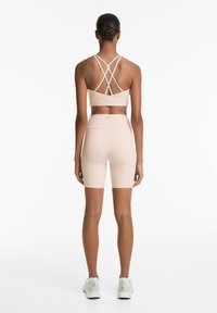 Beige sportos öltözet, amely egy pántos sportmelltartóból és testhez simuló kerékpáros rövidnadrágból áll, sima, rugalmas anyagból készült, finom textúrával.