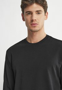 Svart långärmad t-shirt i mjuk bomull. Har en rundad halsringning och en slät yta utan synliga mönster eller detaljer.