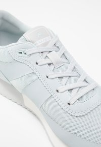 Baskets gris clair en mesh et suède, avec un design à lacets, des panneaux texturés et un logo accentué sur la languette.