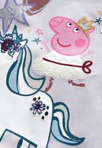 Tissu en coton présentant un personnage de cochon rose portant une couronne et une robe blanche, à côté d'une licorne à crinière bleue avec des accents de broderie florale.
