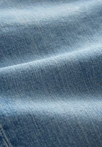 Lichtblauwe denimstof met een zichtbare keperbinding, een zachte textuur en een lichte glans, die subtiele variaties in kleur en patroon laat zien.