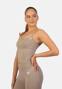Tan activewear crop top met verstelbare bandjes en een getailleerd ontwerp; beschikt over textiel met textuur en een logo-accent aan de linkerkant.