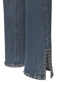 Tumši zili dzinsi ar strukturētām aprocēm, izrotātām ar sudraba kniedēm, sānu šķirbēm un kontrastējošiem diegiem gar šuvēm.