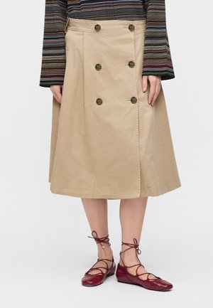 Beige nederdel til knæet med dobbeltradet knapper, båret med bordeauxfarvede snørestøvler og en langærmet, stribet top.