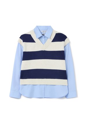 Suéter sin mangas en forma de V a rayas en crema y azul marino sobre una camisa de botones de color azul claro. Tejido de mezcla de algodón, textura suave, diseño en capas.