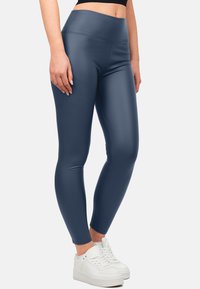 Navyblauwe leggings met een gladde, glanzende textuur en een hoge tailleband, gecombineerd met witte sneakers. Accentstiksels zijn zichtbaar langs de naden.