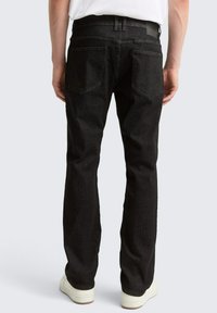 Schwarze Denim-Jeans mit geradem Bein, zwei Gesäßtaschen, Gürtelschlaufen und strukturiertem Stoff, kombiniert mit weißen Sneakern.