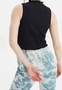 Mustat ribbikuvioiset hihattomat topit, joissa on röyhelökaulus, yhdistettynä vaaleaan sidotun värin housuihin, joissa on sinisiä kuvioita ja joustava vyötärö.