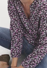 Blouse fleurie avec un fond sombre, ornée de petites fleurs blanches et roses. Coupe ample avec détails de boutons et manches froncées.