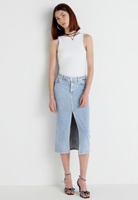 White sleeveless top, light blue denim skirt with front slit, and black heeled sandals with white polka dots and ankle straps.