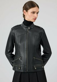Zwarte leren jas met hoge kraag, rits aan de voorkant en twee zijzakken. Voorzien van zilveren hardware en een getailleerd ontwerp.