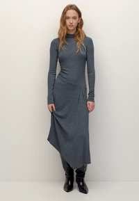 Hosszú ujjú, szürke ruha puha anyagból, aszimmetrikus szegéllyel, testhez simuló felsőrésszel és finom redőzési részletekkel.