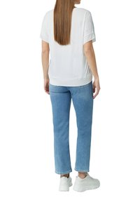 Biała bluzka z krótkim rękawem zestawiona z jasnoniebieskimi dżinsami o prostym kroju i białymi trampkami. Gładka tekstura i prosty design bez widocznych wzorów.